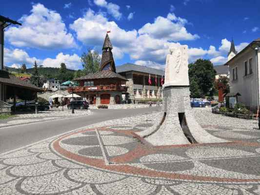Slovensko - vesnička Stará Bystrica - Náměstí - v pozadí Zbojnická Bašta a v popředí je fontána se sochou svatého Michala Archanděla...